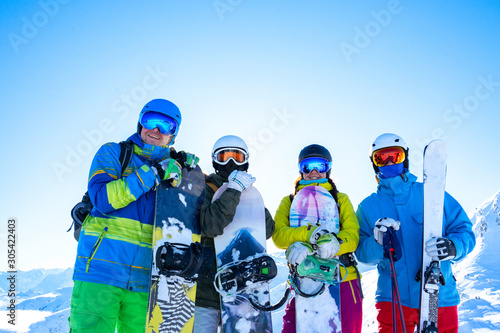Four happy athletes in helmet and with snowboards in their hands at snow resort.