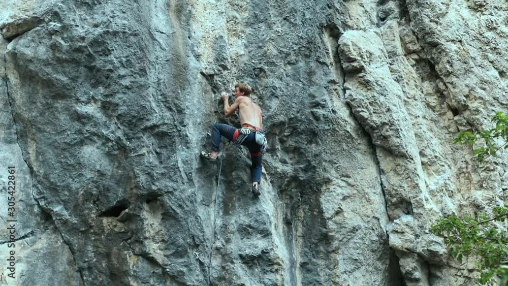 back view strong muscular man rock climber climbing on sport route outdoors on a vertical limestone cliff, making hard wide move, gripping hold and clipping rope. 60 fps slow motion back view strong muscular man rock climber climbing on sport route outdoors on a vertical limestone cliff, making hard wide move, gripping hold and clipping rope. 60 fps slow motion
