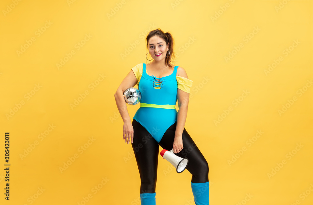 Young caucasian plus size female model's training on yellow background. Stylish woman in bright clothes. Copyspace. Concept of sport, healthy lifestyle, body positive, fashion. Calling with discoball. Young caucasian plus size female model's training on yellow background. Stylish woman in bright clothes. Copyspace. Concept of sport, healthy lifestyle, body positive, fashion. Calling with discoball.