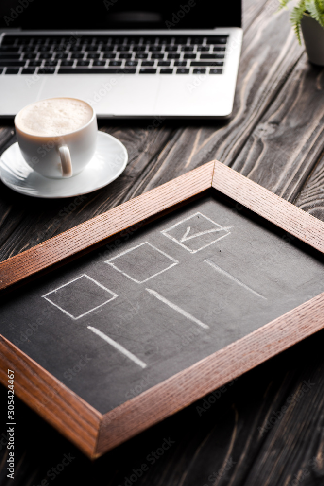 selective focus of chalk board with checklist near cup of coffee and laptop on table, e-commerce concept selective focus of chalk board with checklist near cup of coffee and laptop on table, e-commerce concept