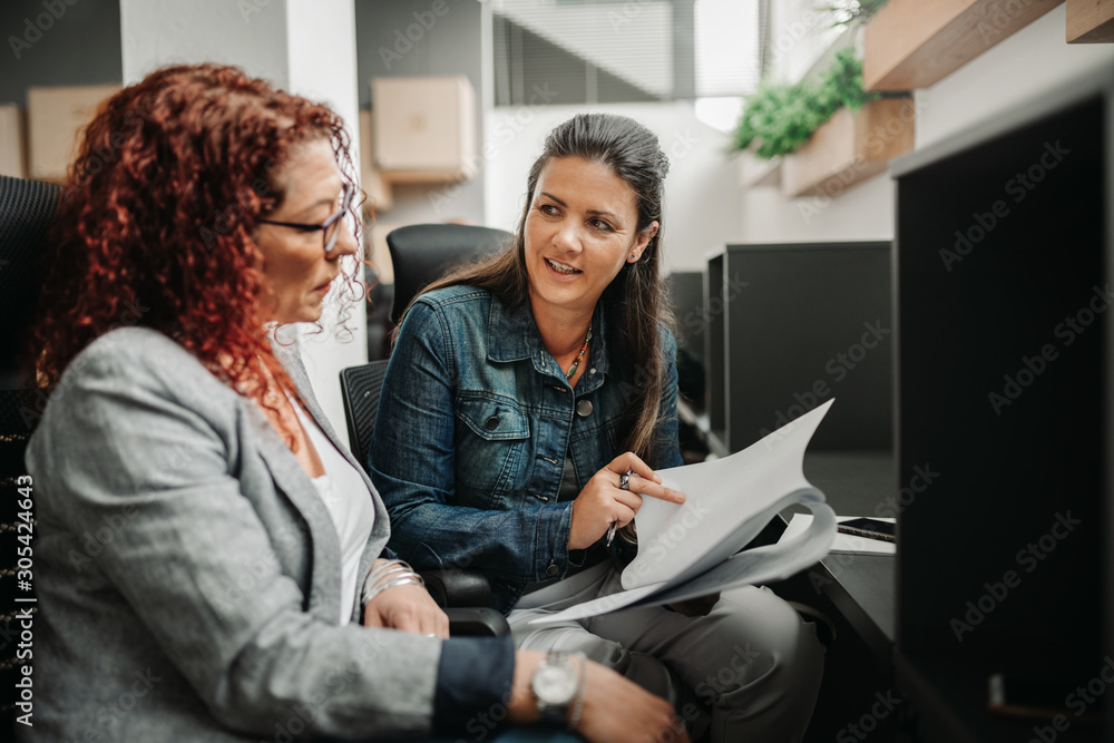 Two businesswoman smiling and talking in a coworking cubicle office space Two businesswoman smiling and talking in a coworking cubicle office space