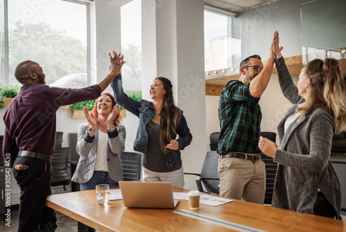 Diverse business team celebrating and giving high fives during boardroom meeting photo