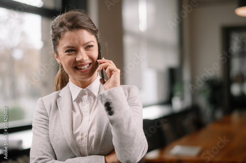 Young businesswoman in office. Beautiful woman talking on smart phone. 