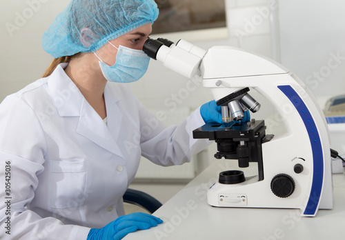 Medical worker looking in microscope and analysing material