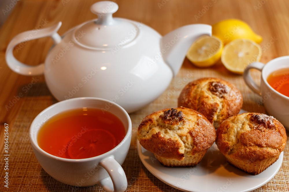 teapot is white and two white cups of tea with lemon and muffins teapot is white and two white cups of tea with lemon and muffins