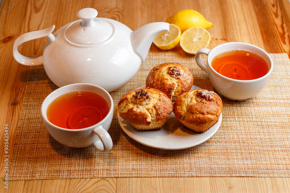 teapot is white and two white cups of tea with lemon and muffins teapot is white and two white cups of tea with lemon and muffins