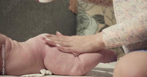 Young mother applying baby powder on little baby buttocks.