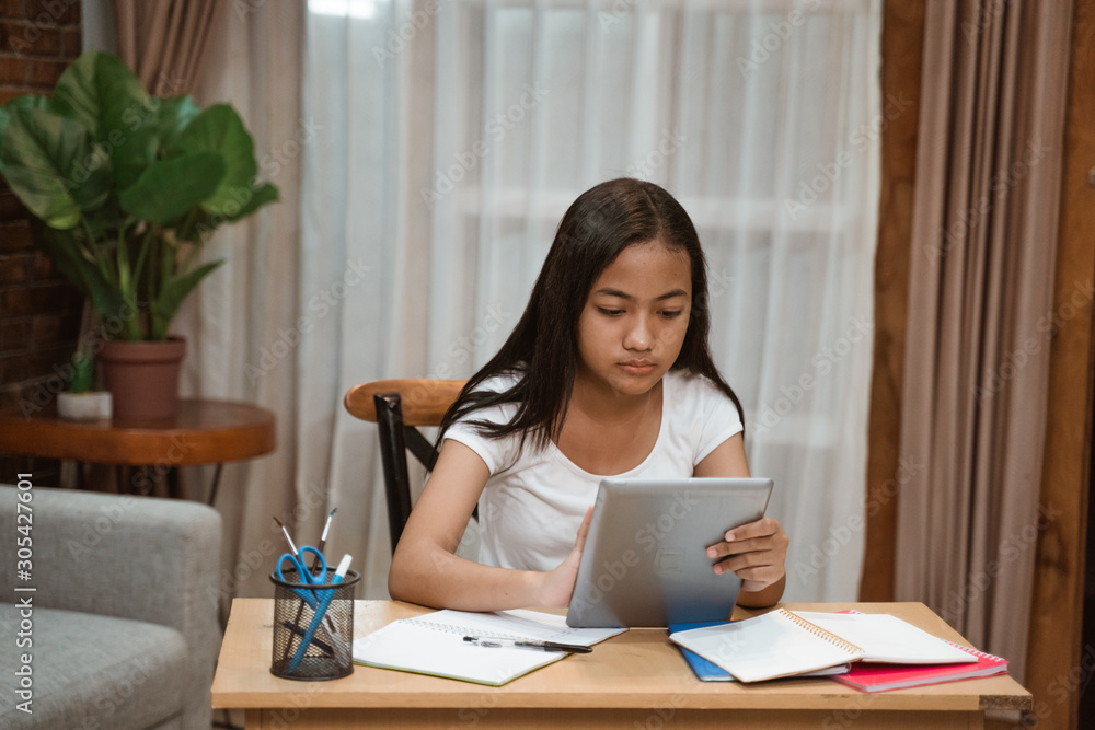 pretty asian teenager doing homework at home using tablet pc pretty asian teenager doing homework at home using tablet pc