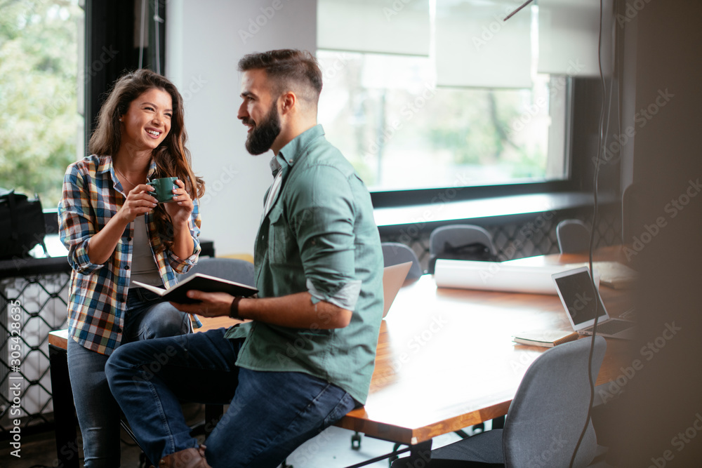 © JustLife - Colleagues in office. Businesswoman and businessman discussing work in office. Two friends in working together.