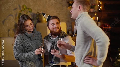 Wallpaper Mural Young man talks to couple in celebrating new years eve party in festively decorated room holding glasses of champagne in hand. Christmas tree with garland in background. Torontodigital.ca