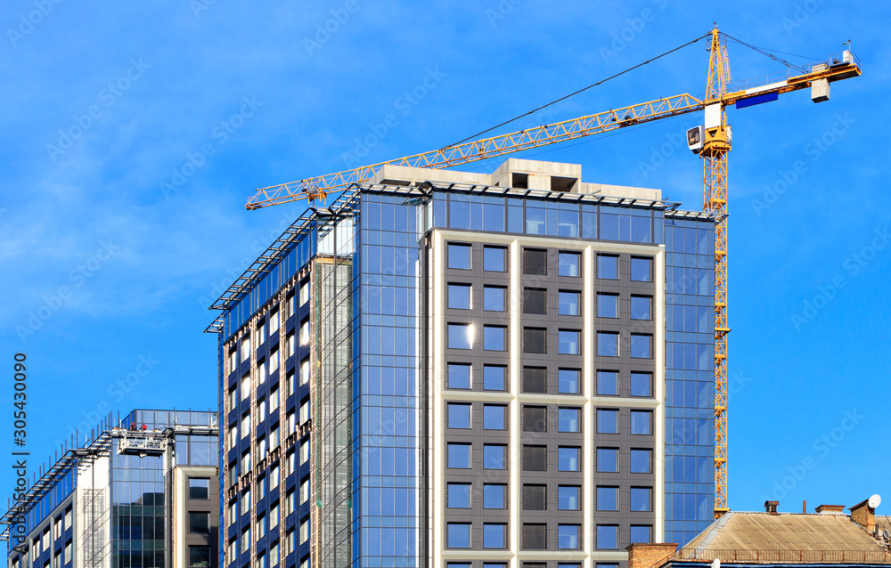 Glass facade, blue sky, crane near a modern concrete building under construction, renovation of old districts. Glass facade, blue sky, crane near a modern concrete building under construction, renovation of old districts.