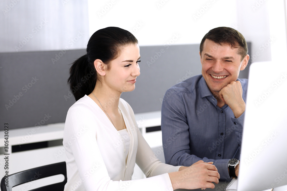 Cheerful smiling businessman and woman working with computer in modern office. Headshot at meeting or workplace. Teamwork, partnership and business concept