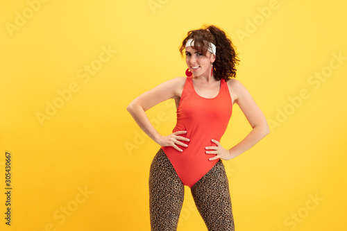 Young caucasian plus size female model's training on yellow background. Stylish woman in bright clothes. Copyspace. Concept of sport, healthy lifestyle, body positive, fashion. Flexible posing.