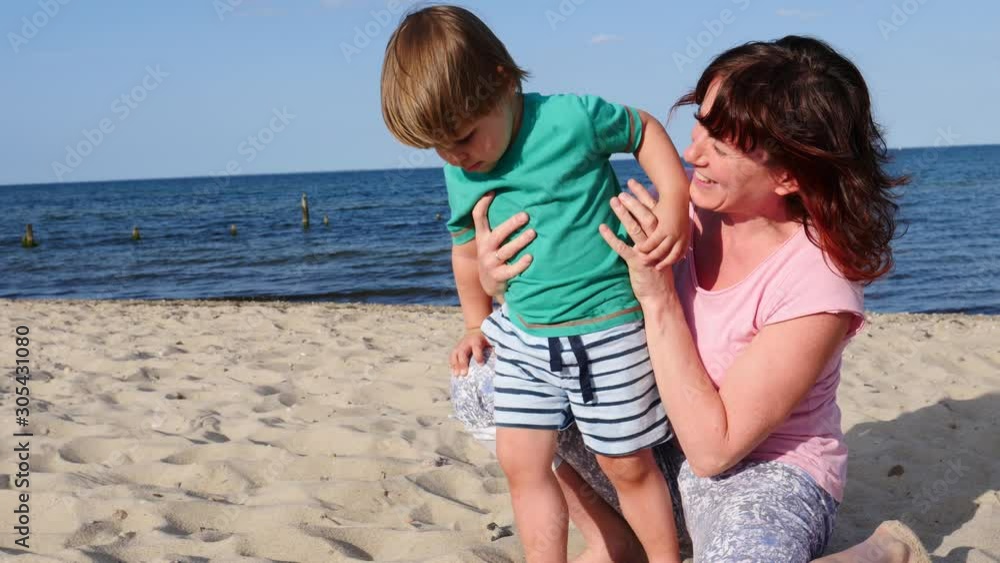 Mother playing with little child boy on sand beach. Adult woman and her son enjoying summer day on seshore. Family holiday at sea. Slow motion Mother playing with little child boy on sand beach. Adult woman and her son enjoying summer day on seshore. Family holiday at sea. Slow motion