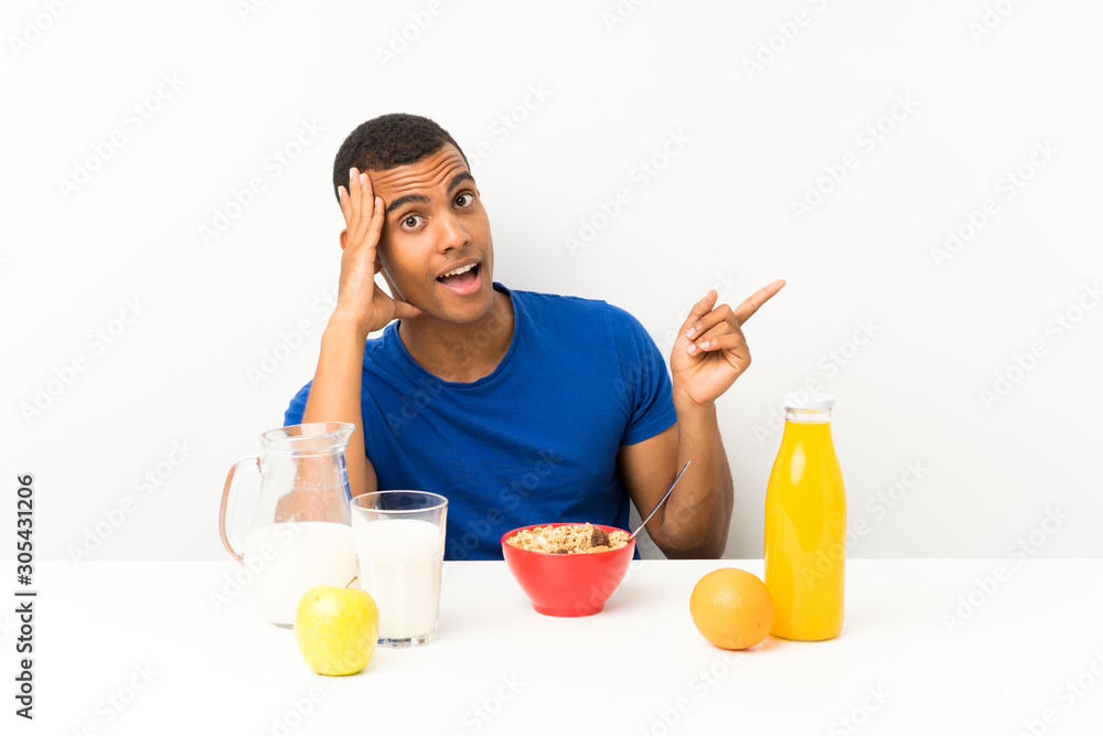 Young man having breakfast in a table surprised and pointing finger to the side