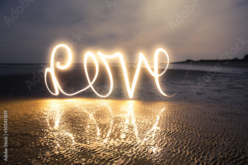 Slika na platnu Light Painting Art: Writing love with light into darkness on the beach at a roma