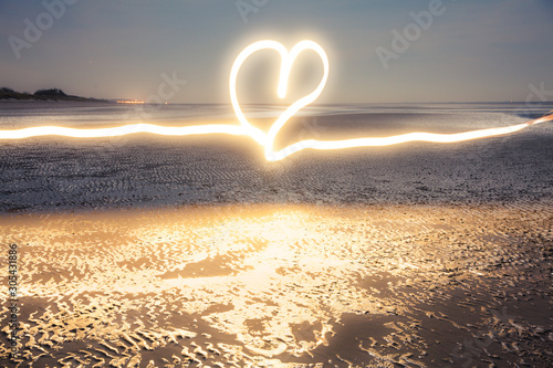 Romantic light painting : Heart drawn with flashlight at blue hour on the beach near the water at low tide