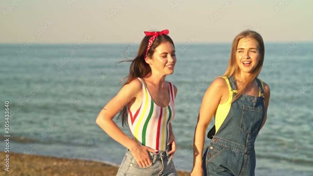 Cheerful two young girls are laughing while walking along the beach in ...