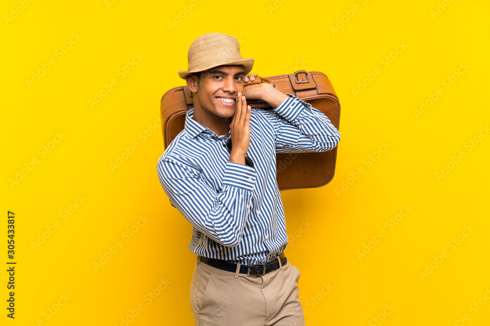 Brunette man holding a vintage briefcase over isolated yellow background whispering something