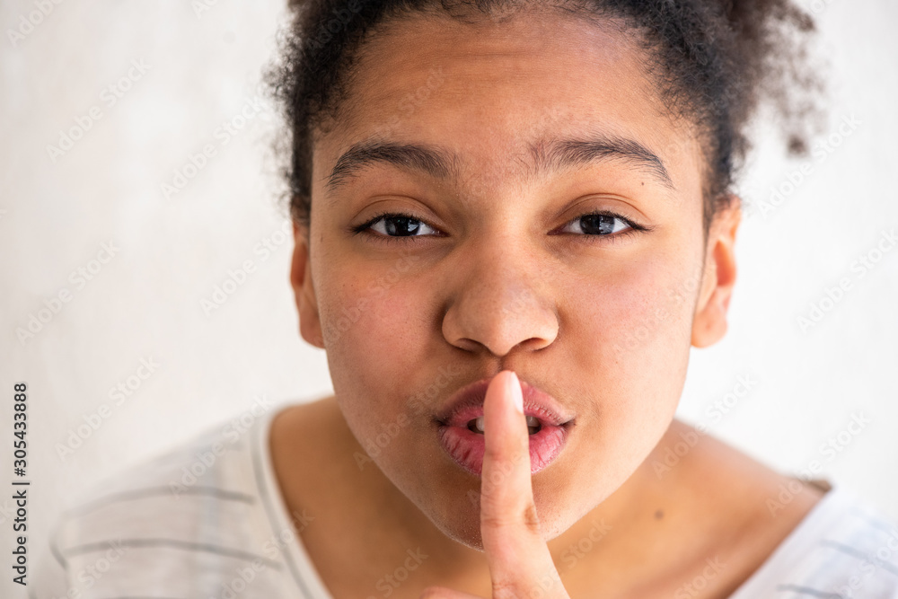 Close up young african american girl with finger to mouth making shh sign Close up young african american girl with finger to mouth making shh sign