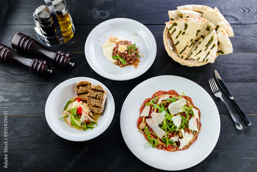 three-course cuisine, carpaccio, tartar and seafood, a set of dishes for dinner on a black table of a restaurant