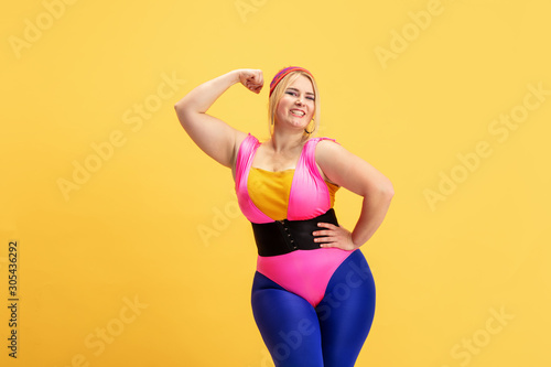 Young caucasian plus size female model's training on yellow background. Copyspace. Concept of sport, healthy lifestyle, body positive, fashion, style. Stylish woman posing and smiling.