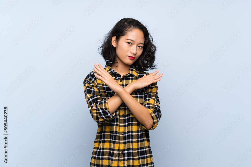 Asian young woman over isolated blue background making NO gesture Asian young woman over isolated blue background making NO gesture