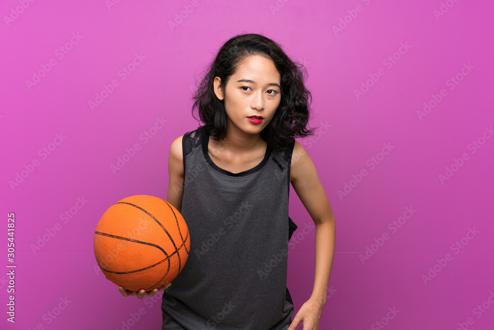 Young Asian woman playing basketball over isolated purple background Young Asian woman playing basketball over isolated purple background