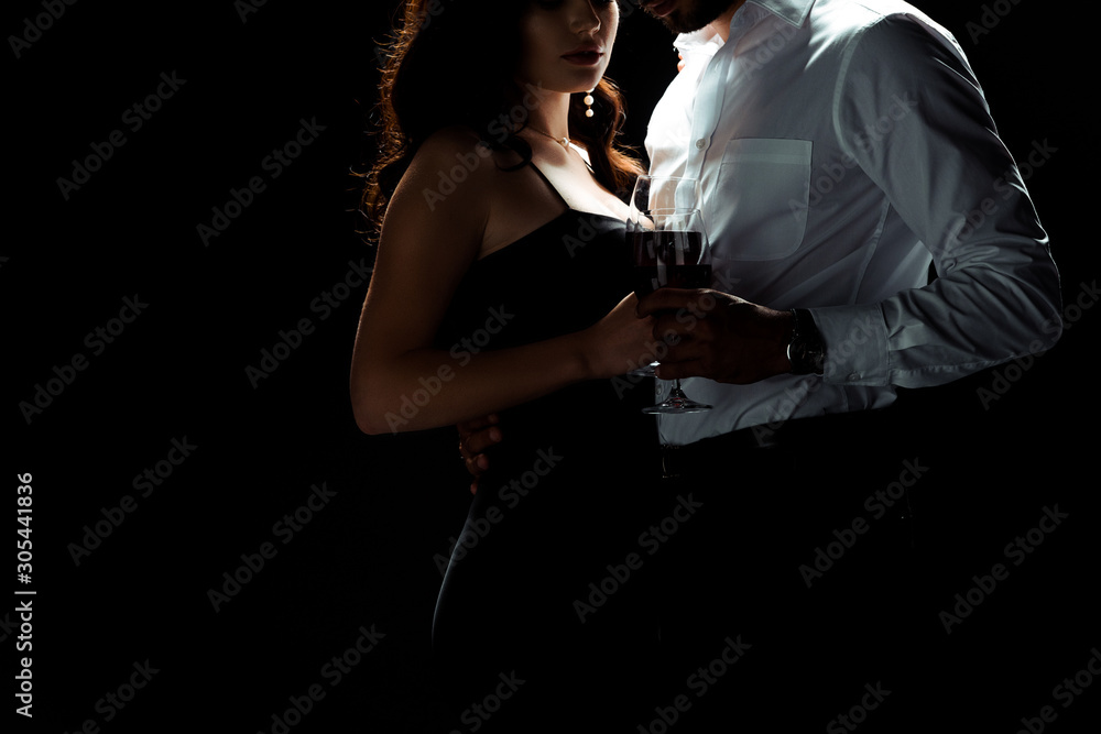 cropped view of bearded man standing with woman holding glass of red wine isolated on black