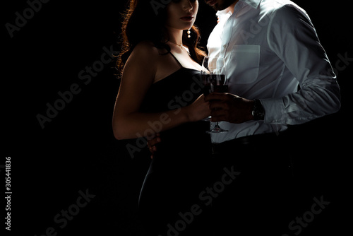cropped view of bearded man standing with woman holding glass of red wine isolated on black