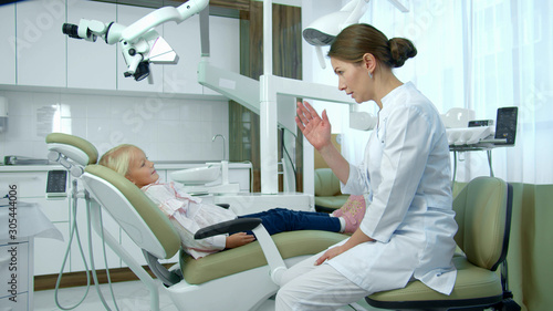 Female dentist talks to a little girl in clinic.
