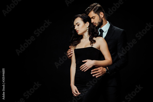handsome bearded man with closed eyes hugging attractive girlfriend isolated on black