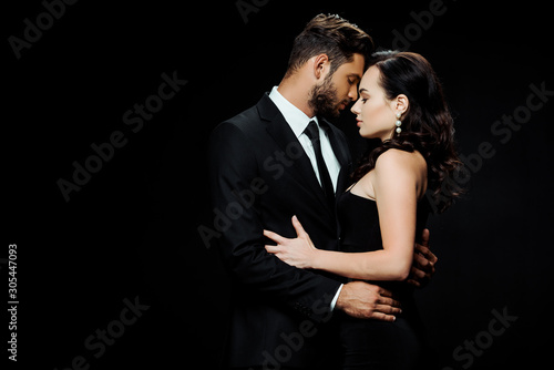 side view of handsome bearded man with closed eyes hugging attractive girl isolated on black
