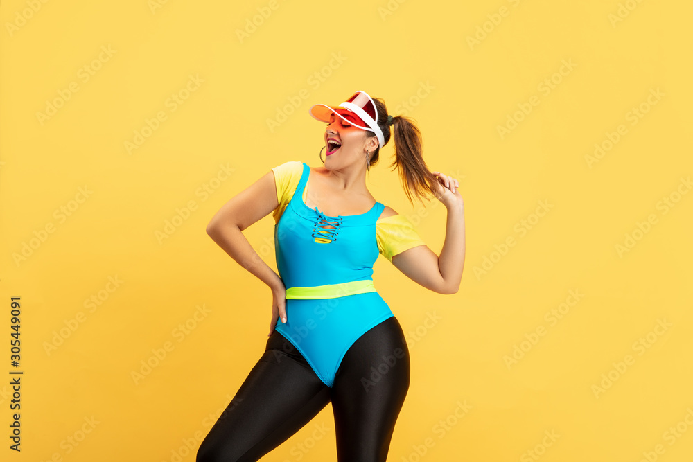 Young caucasian plus size female model's training on yellow background. Copyspace. Concept of sport, healthy lifestyle, body positive, fashion, style. Stylish woman posing confident in red hat. Young caucasian plus size female model's training on yellow background. Copyspace. Concept of sport, healthy lifestyle, body positive, fashion, style. Stylish woman posing confident in red hat.