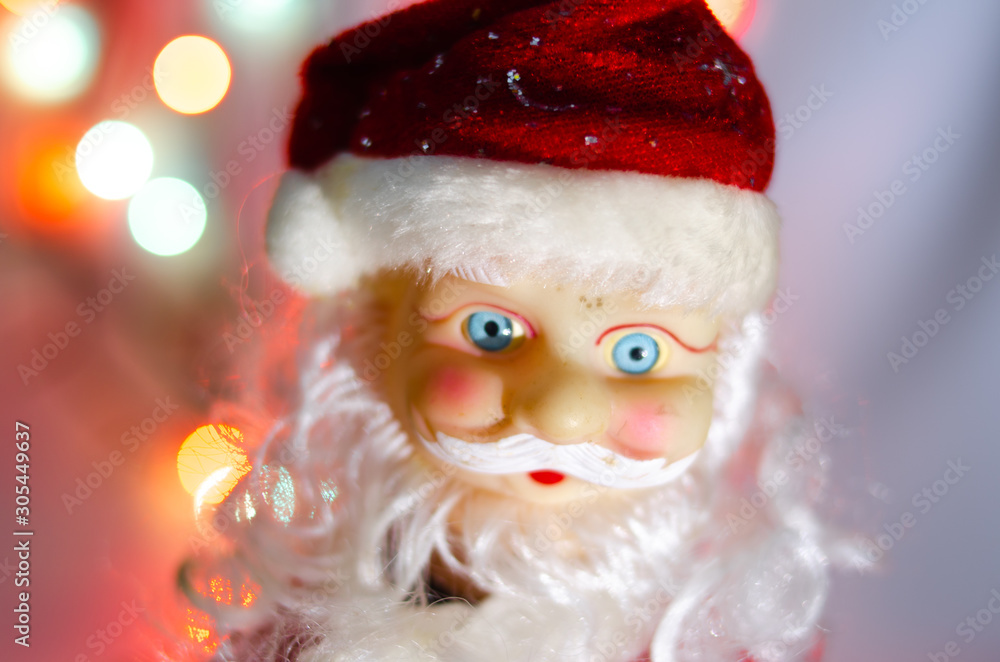Toy, figurine, Santa Claus. Toy Santa Claus on the background of garland lights. Face, parts of the body of Santa Claus. New Year's toy in macro. The suit is red, a large gray white beard. Toy, figurine, Santa Claus. Toy Santa Claus on the background of garland lights. Face, parts of the body of Santa Claus. New Year's toy in macro. The suit is red, a large gray white beard.