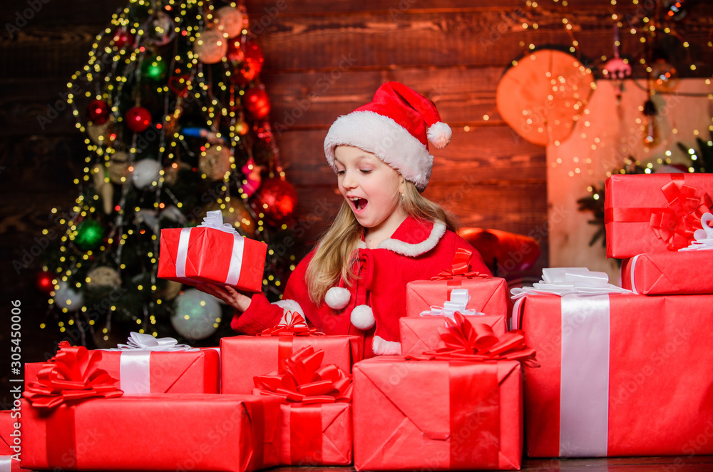 Santa brought me gifts. Child happy excited girl find gifts near christmas tree. Happiness and joy. Merry christmas. Happy childhood concept. Kid wear santa hat hold wrapped christmas gift box