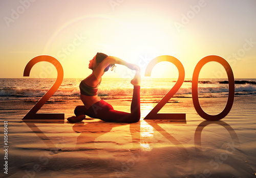 Happy new year card 2020. Silhouette of healthy girl doing Yoga One Legged Pigeon pose on tropical beach with sunset sky background, woman practicing yoga as a part of the Number 2020 sign.