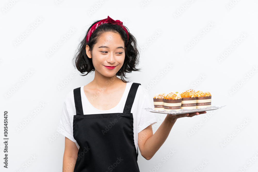 Young asian girl holding lots of muffin cake over isolated white background with happy expression