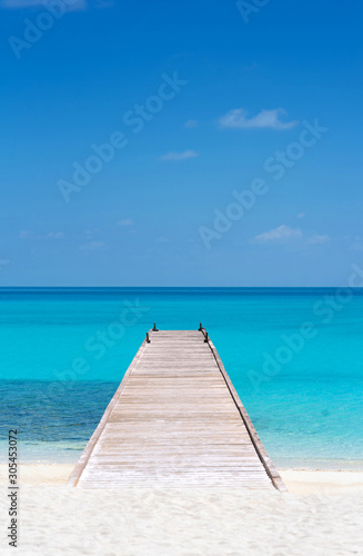 Wooden bridge or pier on tropical white sand beach with clear blue sea and sky on sunny day. Boardwalk into the ocean and turquoise water. Summer holidays background with copy space. Kuramathi Island.