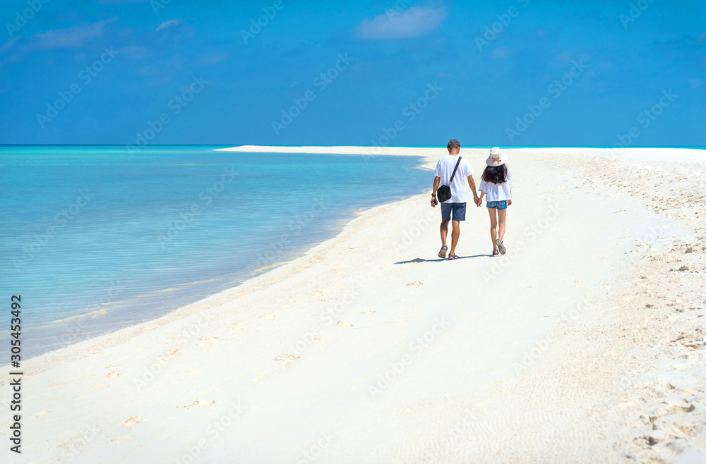 Back view of dad and daughter holding hands enjoy vacation. Asian man and teenager daughter walking side by side on white sand beach with clear blue sea. Concept of friendship and summer vacation time