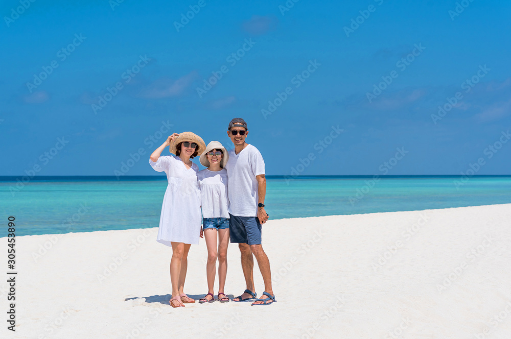 Happy Asian family of three people, mother, father and teenager daughter enjoy summer vacation. Dad, mom, children wearing white clothes, hats, sunglasses stand on white sand beach. Family concept.