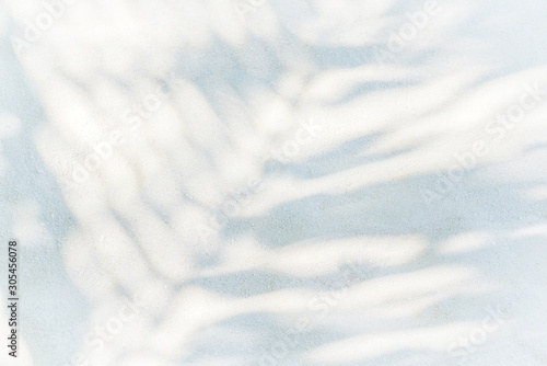 Flat lay or top view of shadows palm leaf on white sand beach texture background. Minimal summer concept with palm tree leaf. Backdrop for mockups and creative advertising, copy space.