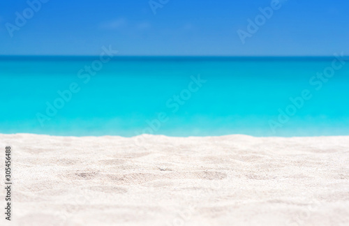 Close up of tropical sand with blurred sea and sky background, summer day. Sandy beach with blurry blue ocean copy space for product.