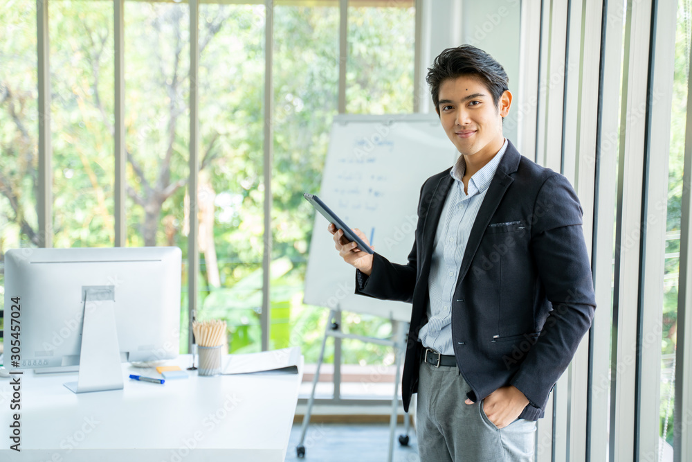 Excited young asian businessman happy and hurrah while standing in the office.Happy Asian man holding tablet and raising his arm up to celebrate success or achievement. Excited young asian businessman happy and hurrah while standing in the office.Happy Asian man holding tablet and raising his arm up to celebrate success or achievement.
