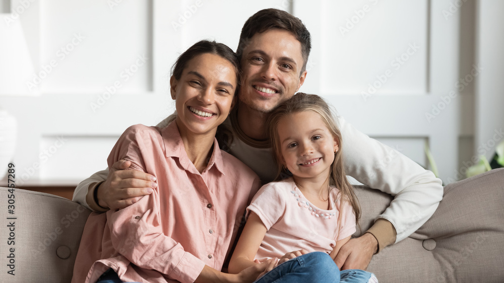 Beautiful young parents with small daughter sit on sofa, portrait Beautiful young parents with small daughter sit on sofa, portrait