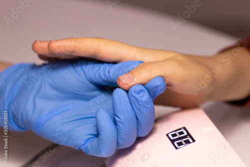 A hand in a blue glove holds the thumb of a client whose skin and nail are smeared with oil.