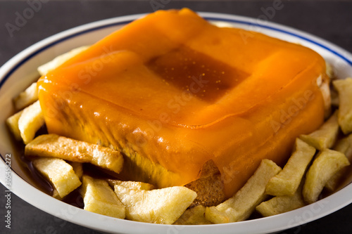 Typical Portuguese francesinha sandwich with french fries on black background. Close up