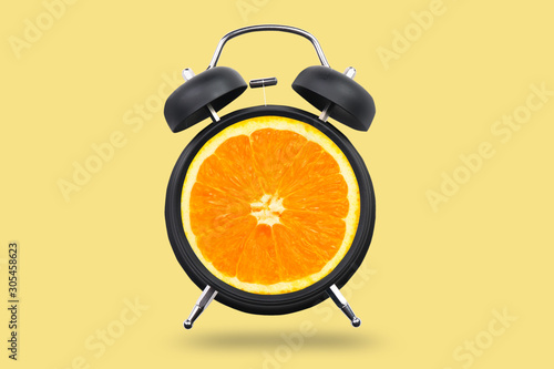 Ripe orange in alarm clock on color background