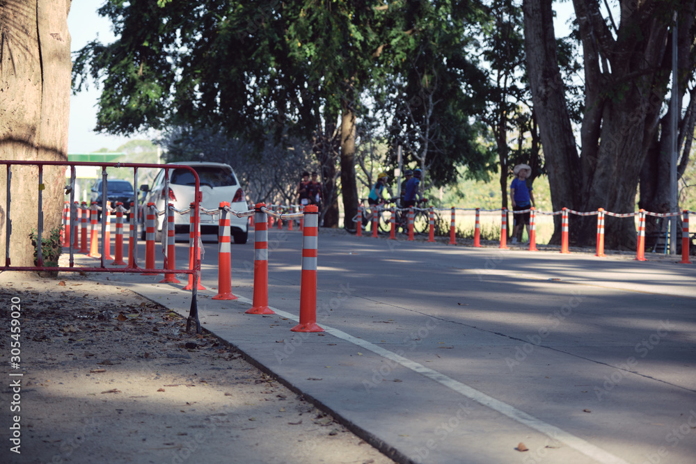 Traffic regulation pole and rumble strip on asphalt road in public park with people exercise background in the evening of sunny day. The symbol of safety first. Traffic regulation pole and rumble strip on asphalt road in public park with people exercise background in the evening of sunny day. The symbol of safety first.