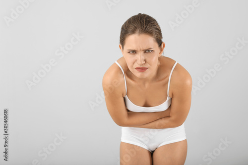 Young woman suffering from abdominal pain on grey background. Gynecology concept